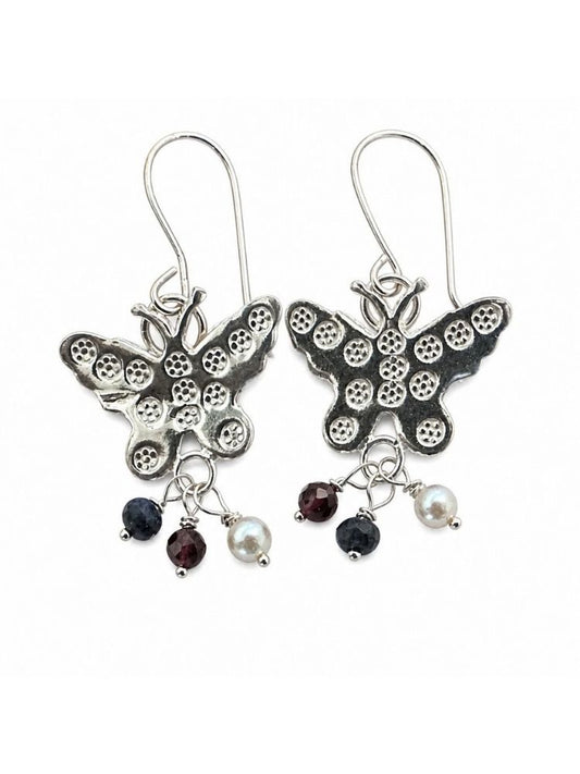 A pair of silver butterfly drop earrings with textured wings, each hanging from a silver fishhook ear wire. Below the butterflies, each earring has three dangling charms: a small dark faceted gemstone, a white pearl bead, and another dark gemstone.