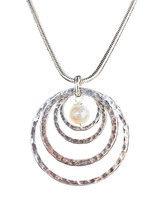 A silver-toned snake chain necklace featuring a pendant with three concentric hammered metal rings and a small, round, lustrous pearl bead at the center, shown against a plain white background.