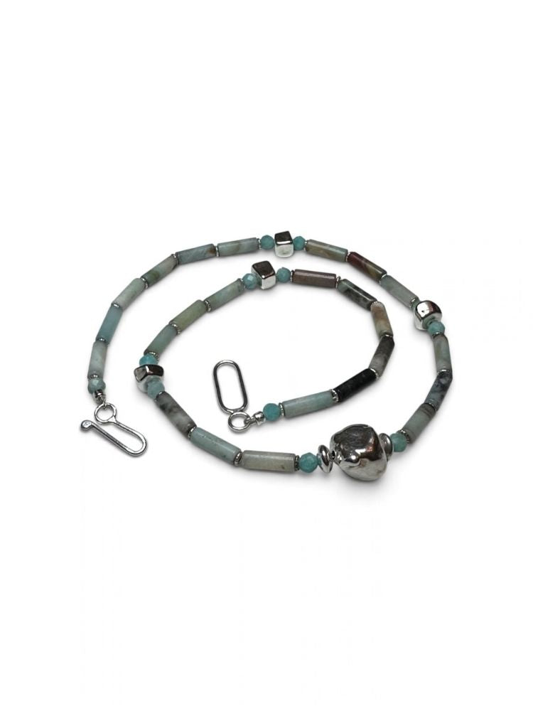 A beaded necklace with cylindrical beads in shades of gray, sage green, and black, accented with small turquoise-blue beads and silver-toned metal spacers, clasp, and a large polished silver bead at the end, displayed on a clean white background.