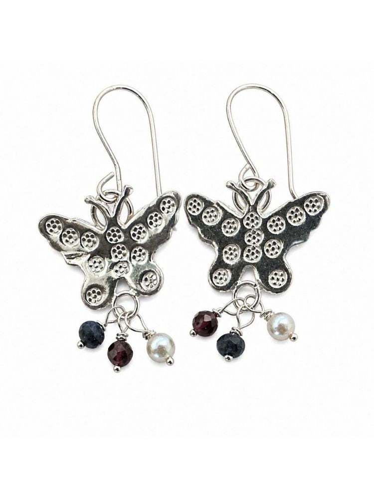 A pair of silver butterfly drop earrings with textured wings, each hanging from a silver fishhook ear wire. Below the butterflies, each earring has three dangling charms: a small dark faceted gemstone, a white pearl bead, and another dark gemstone.