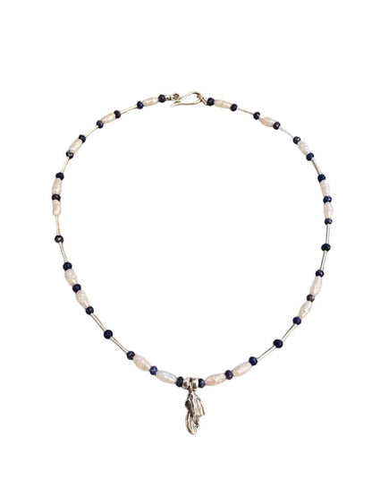 A beaded necklace featuring alternating dark navy blue beads and textured off-white beads, with a small silver-toned feather charm hanging from the center, displayed on a clean white background.