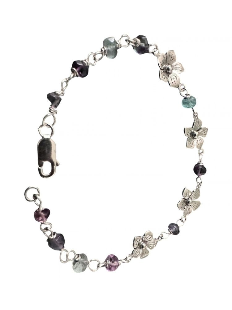 A silver-toned beaded bracelet featuring heart-shaped and flower-shaped charms, accented with faceted beads in purple, gray, and light blue, displayed on a clean white background.