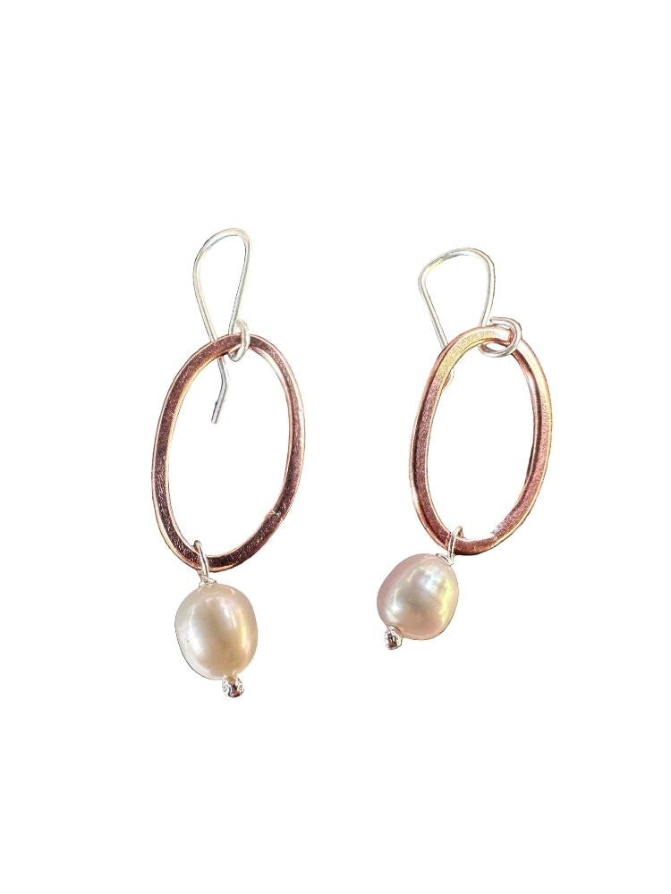A pair of dangle earrings featuring textured rose gold oval hoops with a dangling baroque pearl, suspended from silver fishhook wires, shown against a plain white background.