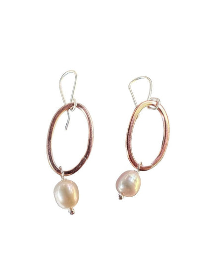 A pair of dangle earrings featuring textured rose gold oval hoops with a dangling baroque pearl, suspended from silver fishhook wires, shown against a plain white background.