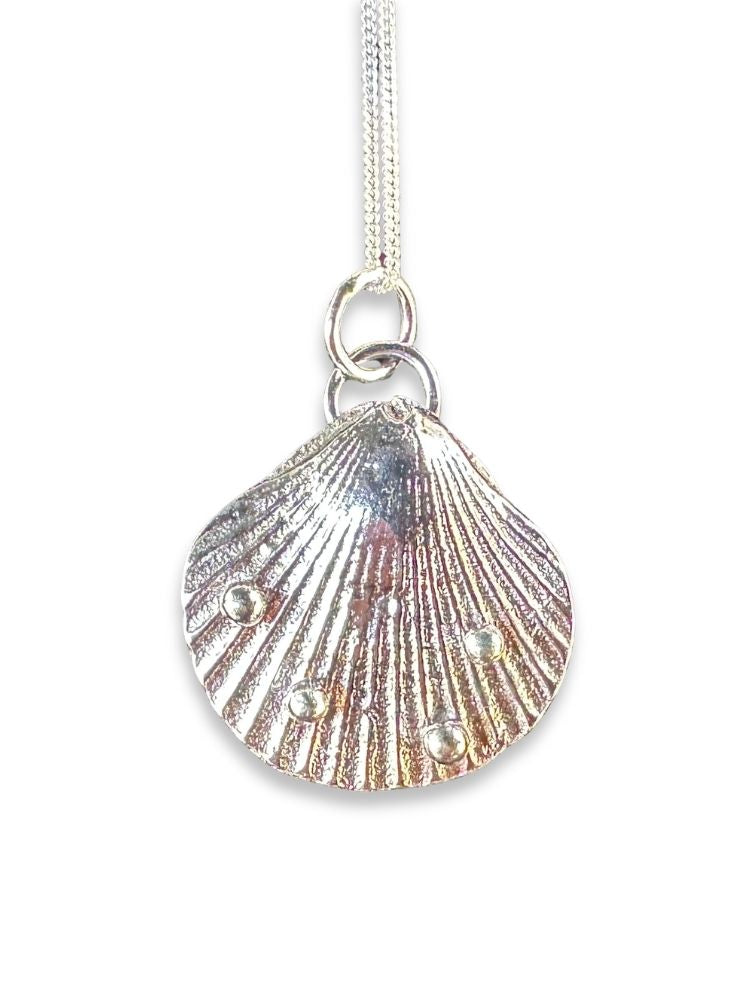A silver-toned shell pendant necklace with a textured scallop pattern and small pearl-like accents, hanging from a silver chain against a white background.
