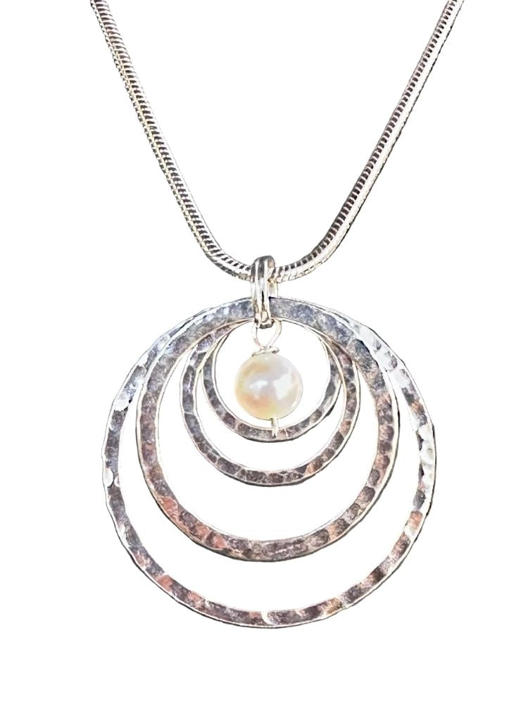 A silver-toned snake chain necklace featuring a pendant with three concentric hammered metal rings and a small, round, lustrous pearl bead at the center, shown against a plain white background.