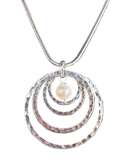 A silver-toned snake chain necklace featuring a pendant with three concentric hammered metal rings and a small, round, lustrous pearl bead at the center, shown against a plain white background.
