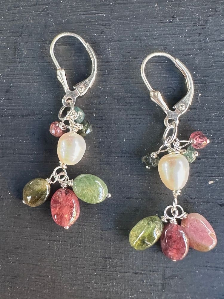 A pair of silver leverback dangle earrings featuring polished multicolor gemstones, including pinkish-red, green, and cream-colored beads, displayed on a dark textured background.