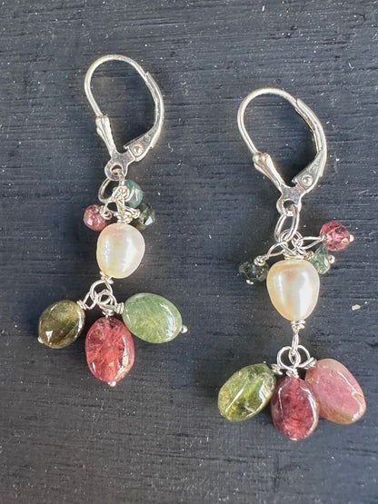 A pair of silver leverback dangle earrings featuring polished multicolor gemstones, including pinkish-red, green, and cream-colored beads, displayed on a dark textured background.